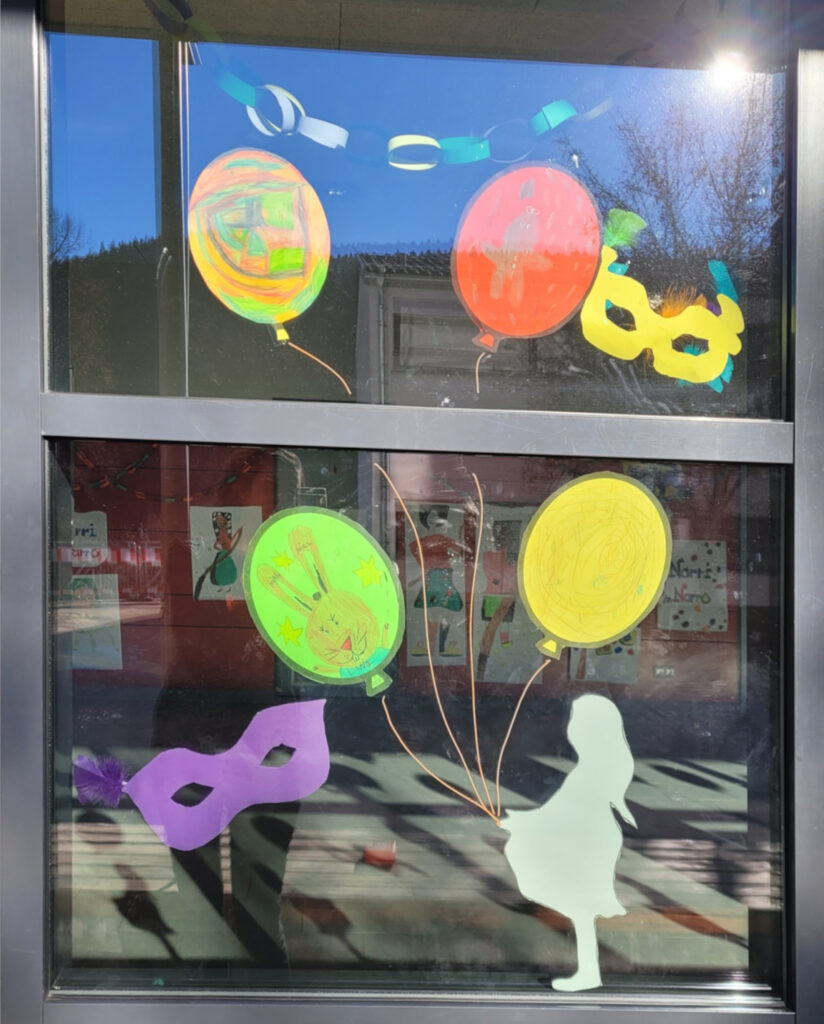 Ein Fensterbild der Silhouette eines Mädchens. Mit ihrer Hand sind mit Schnüren Tonpapier-Luftballons verbunden
