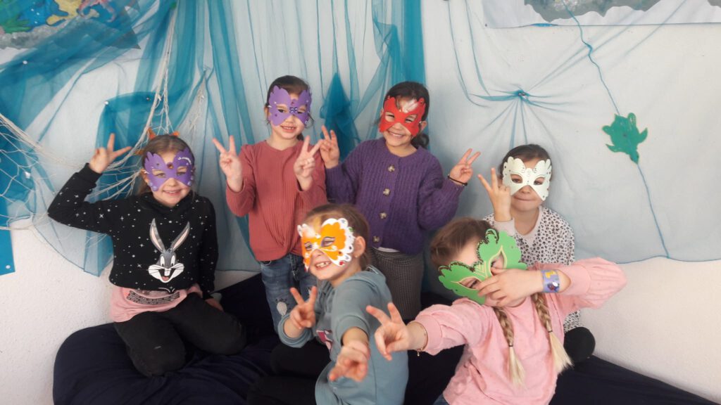 Sechs Mädchen haben Schmetterlings-Masken aus Papier auf und lächeln in die Kamera. 