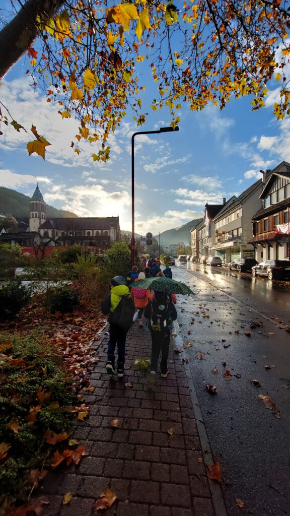 Kinder gehen mit Regenschirmen eine regennasse Straße entlang